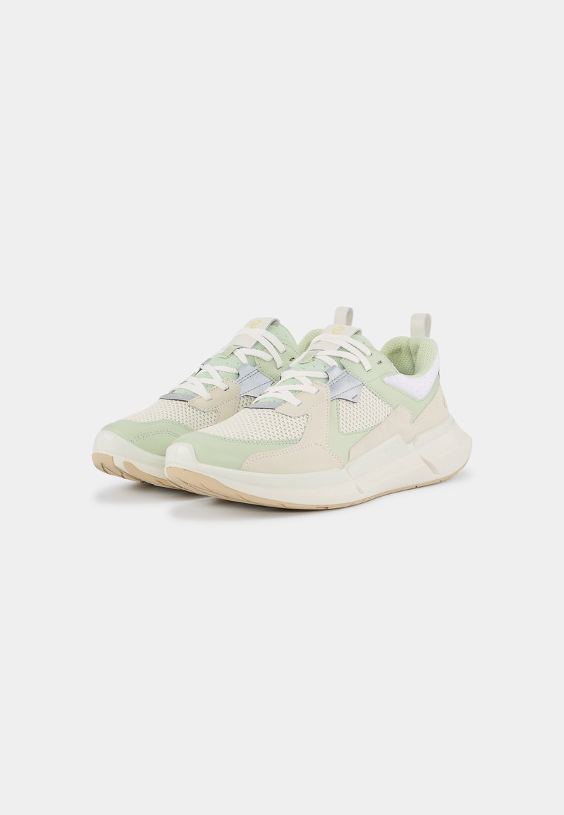 Sneaker mit einem leicht grünen und cremefarbenen Obermaterial, aus Mesh und glatten Materialien, weißen und grauen Akzenten sowie einer dicken, beigen Gummisohle.