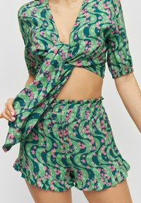 Top corto floreale verde con davanti annodato e maniche a palloncino, abbinato a pantaloni corti coordinati con orlo arricciato e un design stampato simile.