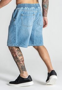 Shorts de mezclilla azul claro con una cinturilla elástica, dos bolsillos traseros y un ajuste holgado. Llevados con zapatillas negras con una suela blanca.