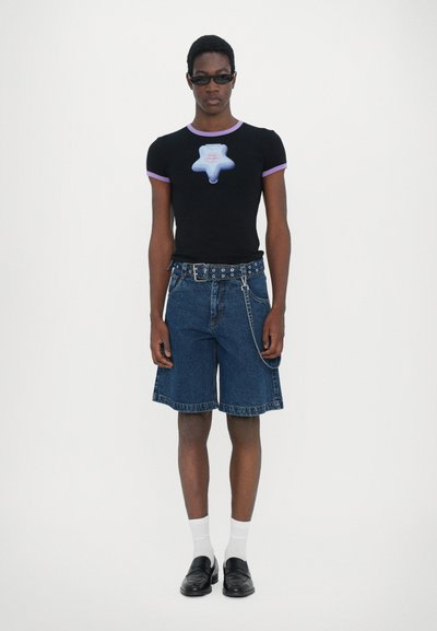 T-shirt noir avec une bordure violette et un imprimé graphique, associé à un short en denim foncé avec un détail en chaîne et une ceinture avec des trous ronds.