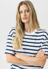 T-shirt rayé blanc avec des rayures bleu marine, col rond, manches courtes, coupe décontractée, texture lisse. Le mannequin pose avec les bras croisés.