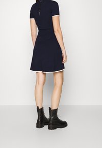 Robe en tricot marine à manches courtes, avec des bordures blanches et une jupe évasée, associée à des bottes de combat noires à lacets. Détail zippé au dos.