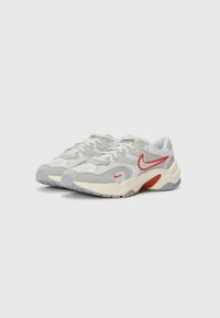 Grijze sportschoenen met een bovenwerk van mesh en suède, witte accenten, een rode Nike swoosh en een contrasterende crème en grijze zool.