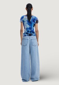 Plava široka majica kratkih rukava s tie-dye uzorkom u plavim nijansama uparena s svijetloplavim širokim trapericama. Majica ima meku, lepršavu teksturu i okrugli izrez.