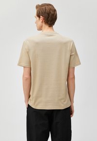 Camiseta de algodón beige de manga corta y cuello redondo, con un diseño simple y textura suave. Se muestra vista trasera.
