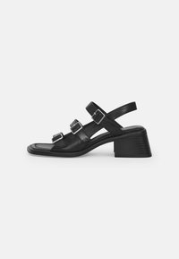 Black leather sandal with three adjustable buckle straps, a square toe, and a tapered block heel. Smooth texture and minimalistic design.