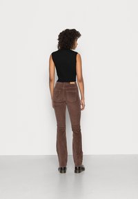 Pantalons en velours côtelé marron évasés avec une taille haute, quatre poches et une étiquette à l'arrière. Assortis avec un haut noir sans manches en maille côtelée.