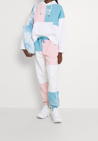 Sudadera con capucha en azul, rosa y blanco con un gran bolsillo frontal; combinada con joggers pastel a juego. Zapatillas blancas y un tote de tie-dye.