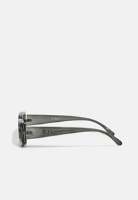 Gafas de sol grises con lentes rectangulares, montura de plástico y varillas delgadas. Presentan una marca en las varillas y un acabado mate.