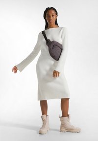 Rochie tricotată albă cu dungi, cu mâneci lungi, asociată cu cizme bej cu șireturi și căptușeală, și o poșetă pufoasă mov crossbody. Textură fină a materialului.