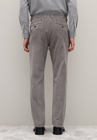 Grijze corduroy broek met verticale geribbelde textuur, voorzien van achterzakken met knopen, gedragen met een grijs overhemd met patroon en zwarte schoenen.