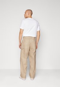 Beiga cargobyxor med lös passform, som har två stora bakfickor, vita sömnadsdetaljer och en slät tygtextur, i kombination med en enkel vit t-shirt.