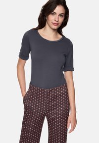 Graues eng anliegendes T-Shirt mit kurzen umgeschlagenen Ärmeln, kombiniert mit gemusterten roten und marineblauen Hosen mit Rautenmuster und seitlichen Taschen.