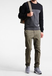 Mörkgrå och svart sweatshirt med rund hals, kombinerad med olivgröna chinos och grå sneakers. Väskan är ljusgrå med axelremmar.