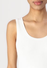 White cotton tank top with a rounded neckline and wide straps. Smooth texture and fitted shape, designed for comfort and layering.