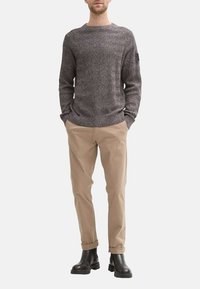 Pull en maille texturé gris avec un col rond, associé à un chino beige et des bottines noires. Le pull présente de subtils motifs en chevrons.