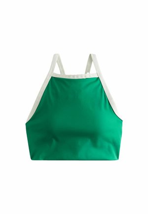 Ung kvinde med krøllet hår iført en grøn ærmeløs crop top med hvid kant, der kigger let opad og til siden.