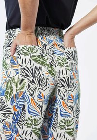 Elastische taillebroek met een lichtcrème basis, voorzien van een levendig botanisch patroon in groen, blauw en oranje; inclusief zijzakken.