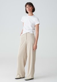 White short-sleeve t-shirt with a round neckline paired with beige pleated wide-leg trousers. Footwear features a contrasting black sole.