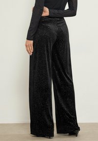 Zwarte fluwelen wijde broek met een gestructureerde stof en verspreide zilveren stippen, hoge taille en vloeiende silhouet.