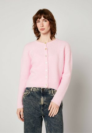 Roze, fluffy cardigan met een ronde halslijn en zeven knopen aan de voorkant. Lichtgewicht textuur vormt een contrast met de donkerblauwe gebloemde jeans.