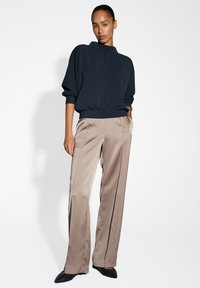 Maglione navy con colletto alto e orlo elastico, abbinato a pantaloni beige chiaro con cuciture verticali e vestibilità rilassata, indossato con tacchi neri.