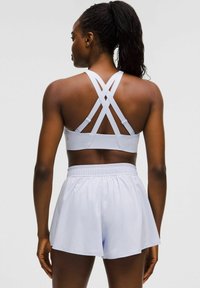 Sostenedor deportivo blanco con tirantes entrecruzados; combinado con pantalones cortos de textura suave en azul claro con cinturilla elástica.