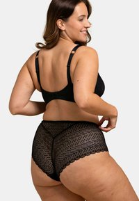 Set de lingerie en dentelle noire comprenant un soutien-gorge texturé avec des bretelles réglables et une culotte taille haute semi-transparente à motifs avec des bords festonnés.