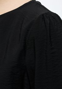 Tissu noir texturé avec un large décolleté carré et une manche ballon froncée à l'épaule.