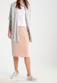 Ljusgrå öppen cardigan, vit t-shirt, rosa pennkjol och metalliska guldskor, med släta ytor och en avslappnad passform.