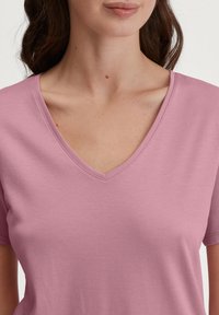 Lichtroze T-shirt met korte mouwen en V-hals, gemaakt van zachte stof, met een gladde textuur en een eenvoudige silhouet.