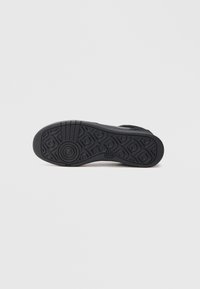 Suela de zapatilla negra con una superficie de goma texturizada que presenta patrones circulares y ondulados, diseñada para ofrecer agarre y durabilidad.