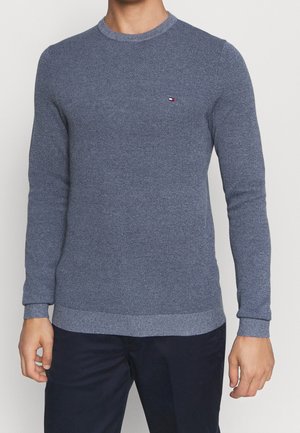 Blauer strukturierter Strickpullover für Herren mit kleinem Tommy Hilfiger-Logo auf der linken Brust, kombiniert mit dunkelblauen Hosen.