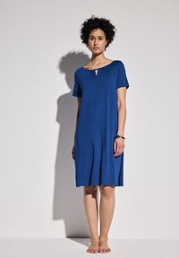 Niebieska sukienka z krótkim rękawem, okrągłym dekoltem i detalem w postaci dziurki. Wykonana z lekkiego materiału, ma luźny krój, sięgający do połowy uda.