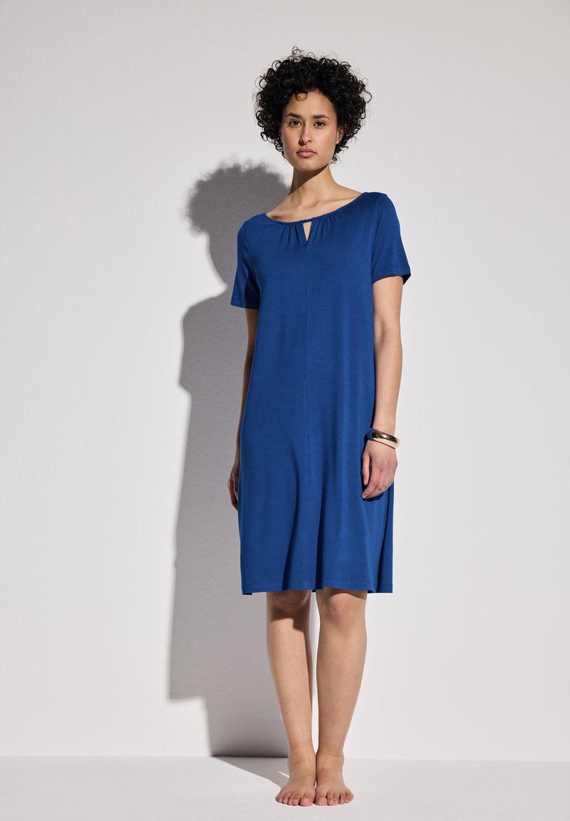 Niebieska sukienka z krótkim rękawem, okrągłym dekoltem i detalem w postaci dziurki. Wykonana z lekkiego materiału, ma luźny krój, sięgający do połowy uda.