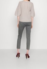 Pull en maille beige clair avec des manches ballons texturées, associé à un jean gris fuselé et des chaussures à talons bordeaux avec un design tissé.