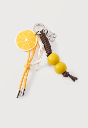 Sleutelhanger met gele citroenschijf bedel, gele koorden, bruin gewikkeld koord, twee gele kralen en een zilveren metalen sluiting met logobedel.