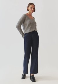 Grå strikket sweater med en bred udskæring, parret med mørkeblå højtaljede vide bukser. Outfittet er afsluttet med sorte platform sko.
