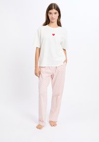 Biały bawełniany t-shirt z czerwonym wzorem serca, zestawiony z jasnoróżowymi spodniami do spania z małymi czerwonymi kropkami.