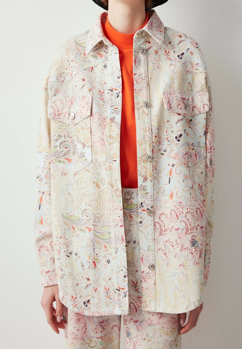 Surchemise légère à motifs dans des tons pastel avec des motifs floraux, des boutons-pression et deux poches poitrine, associée à un haut orange vif.