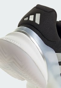 Μαύρο αθλητικό παπούτσι με επάνω μέρος από υφασμάτινο υλικό με υφή, ασημί λεπτομέρειες και διάφανη λαστιχένια σόλα με ζιγκ ζαγκ μοτίβο.