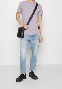 Fialové bavlněné tričko, černá crossbody taška, světle modré ošuntělé džíny a černé šněrovací boty s chunky podrážkou. Jednoduchý design, ležérní styl.
