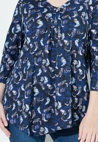 Camisa azul con un fondo a cuadros oscuros decorado con botas de vaquero y espuelas en tonos púrpura claro y blanco, combinada con jeans azules.
