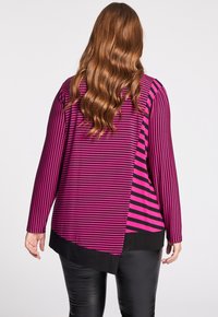 Långärmad topp med horisontella ränder i varierande nyanser av rosa. Svart fåll och sidor skapar kontrast mot det randiga mönstret.