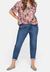 Blusa rosa con motivo floreale e maniche corte, abbinata a jeans blu arrotolati e ballerine verdi. Tessuto piatto e liscio con vestibilità rilassata.