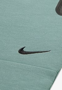 Vêtement Nike en tissu bleu clair, doté d'un tricot texturé, avec un logo swoosh noir brodé en évidence sur la surface.