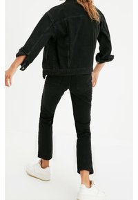 Chaqueta de mezclilla negra con mangas enrolladas, combinada con jeans negros de corte slim. Incluye zapatillas blancas; diseño simple, sin patrones ni acentos visibles.