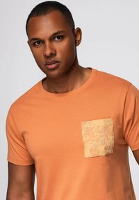 Oranžové tričko s čtvercovou kapsou z vzorované světle oranžové látky. Hladká textura a krátké rukávy, design s límcem.