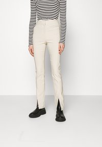 Beige kalhoty na míru se bočními rozparky, s vysokým pasem a slim fit střihem. Nosené s černobílým pruhovaným topem a černými botami.