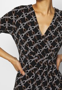 Robe noire présentant un motif répétitif de maillons de chaîne en blanc et rouille. Le tissu a une texture douce, avec un col en V et des manches courtes.